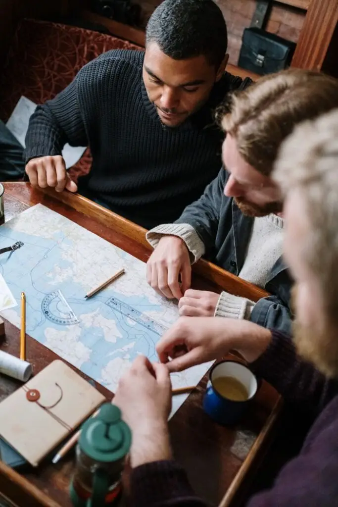 Three men discussing route planning using a maritime map aboard a wooden table.